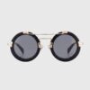 Round black and gold sunglasses displayed against a neutral background, showcasing their stylish design and color contrast.