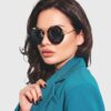 A woman in sunglasses and a blue blazer stands confidently, showcasing a stylish and professional appearance.