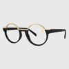 A pair of eyeglasses featuring gold rims and black frames, resting on a flat surface.