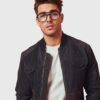 A man wearing glasses and a jacket, standing confidently with a neutral expression.