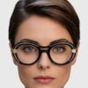 A woman with black-framed glasses, looking directly at the camera with a neutral expression.