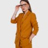 A woman wearing a mustard-colored suit and glasses, standing confidently with a neutral background.