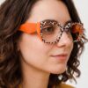 A woman wearing stylish orange cat-eye glasses, smiling and looking directly at the camera.