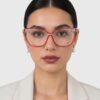 A woman with red glasses and a white blouse smiles, showcasing her stylish eyewear and professional attire.