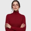 A woman with glasses wearing a red turtleneck sweater, smiling and looking directly at the camera.