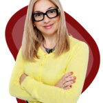 A woman wearing glasses and a yellow shirt smiles at the camera, showcasing her friendly demeanor.