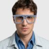 A man with glasses featuring a blue frame, looking directly at the camera with a neutral expression.