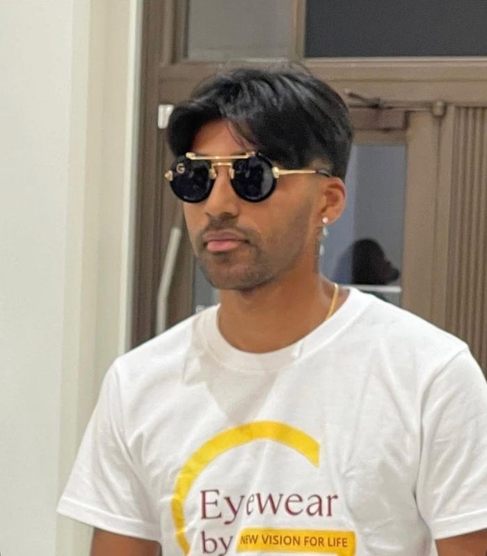 A man wearing sunglasses and a white t-shirt, standing outdoors with a neutral expression.