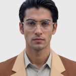 A man in a tan suit and glasses stands confidently, showcasing a professional appearance.