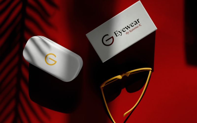 A pair of sunglasses and a business card are placed on a vibrant red surface, creating a striking visual contrast.